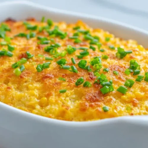 cheesy corn casserole baked golden with chives in a white dish